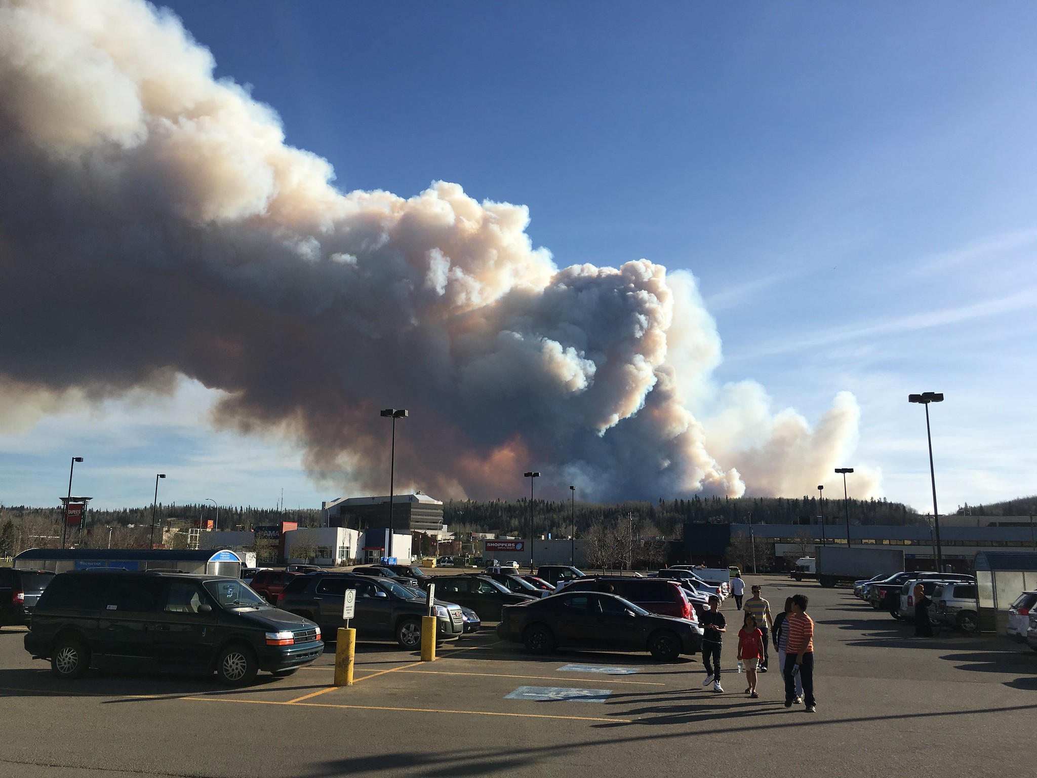 People in a parking lot with large plume of wildfire smoke in background